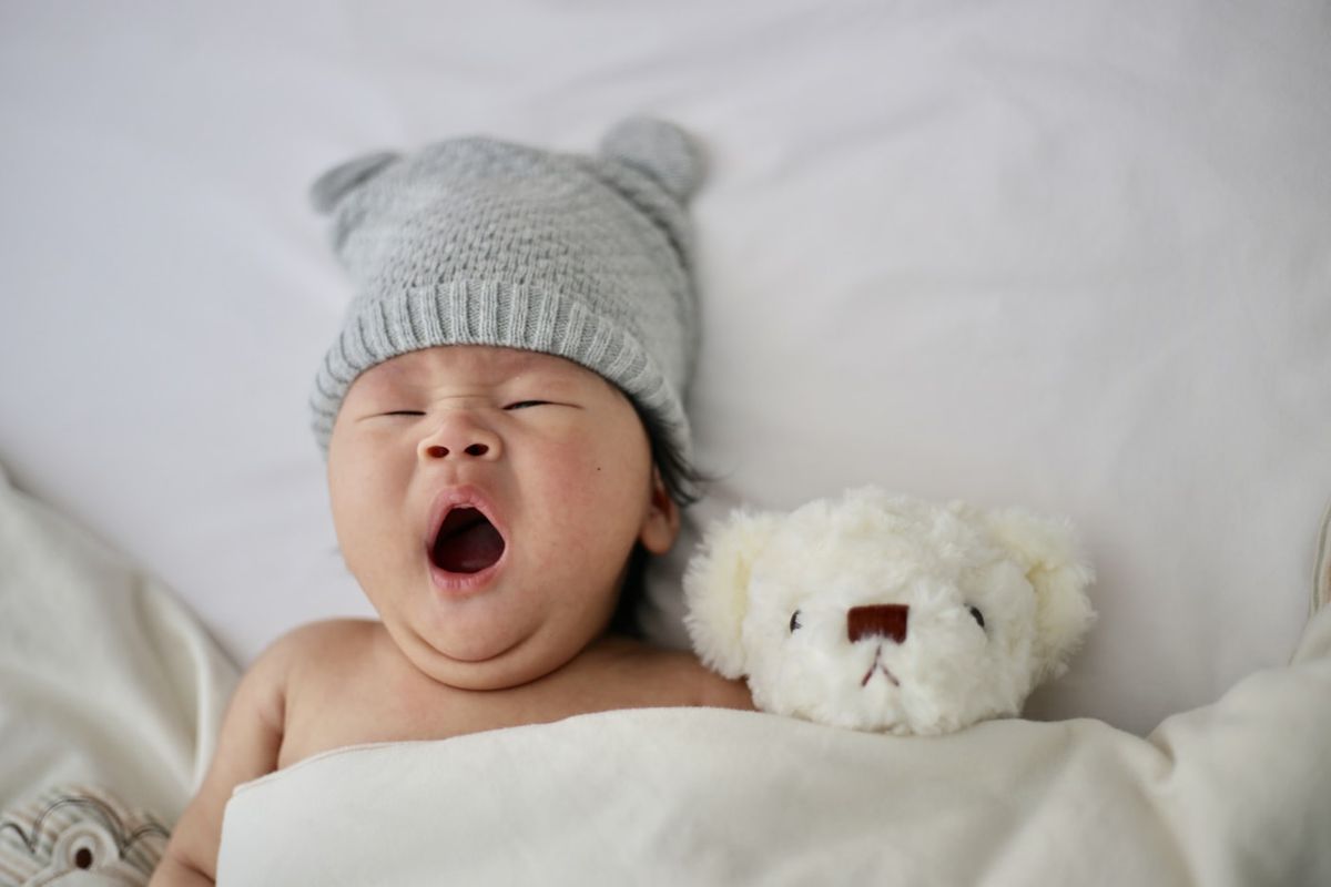Spedbarn med lue ligger i sengen med en kosebamse
